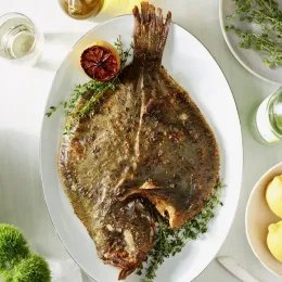 Whole roasted turbot fish on plate with lemon and herbs