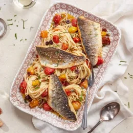 Four branzino fish fillets on top of spaghetti and cherry tomatoes on platter