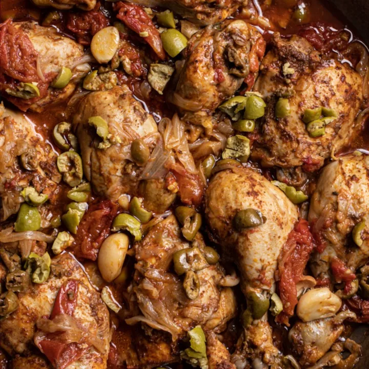 Close up shot of chicken pieces in red sauce with chopped green olives.