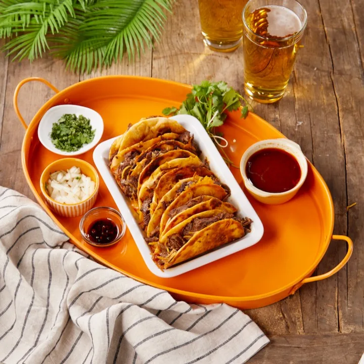 Beef tacos on orange platter with toppings and beer