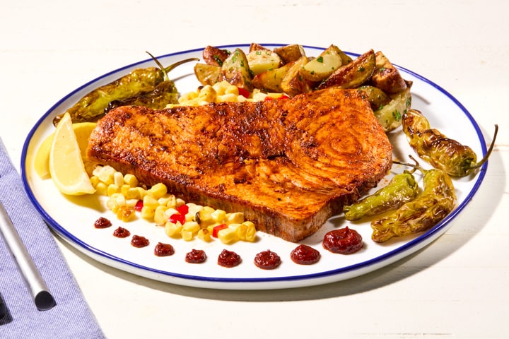 Harissa swordfish steak with blistered shishito peppers, corn, and lemon on a platter