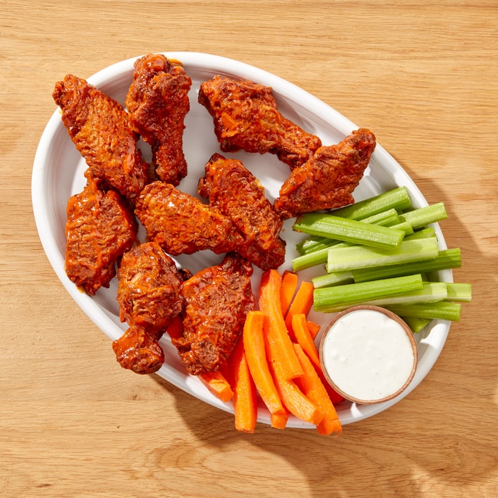 Air fryer buffalo wings with celery and carrot sticks and creamy dressing on platter.